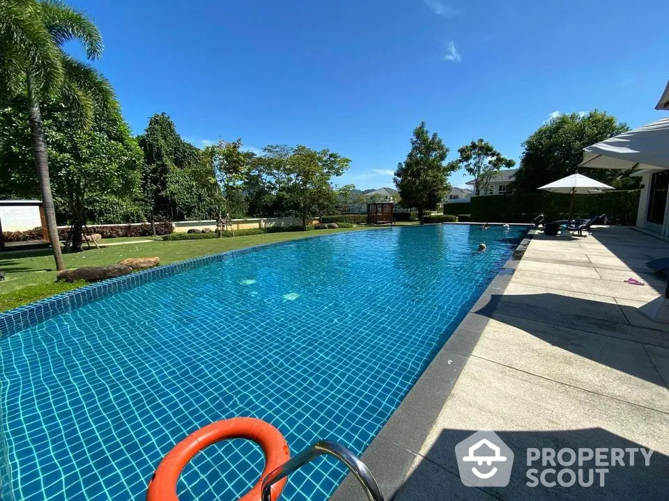 Luxurious outdoor swimming pool with lush greenery and clear blue sky, perfect for relaxation and leisure.