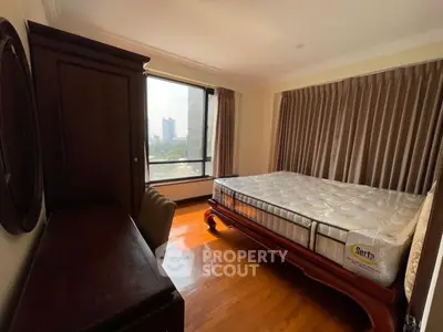 Spacious bedroom with large window and elegant wooden furniture in urban apartment.