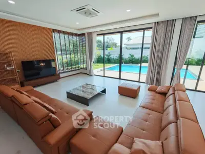 Luxurious living room with pool view, featuring modern leather sofas and floor-to-ceiling windows.