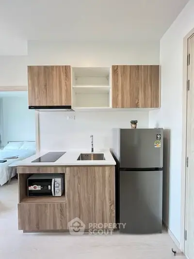 Modern compact kitchen with wooden cabinets and stainless steel appliances in a cozy apartment.