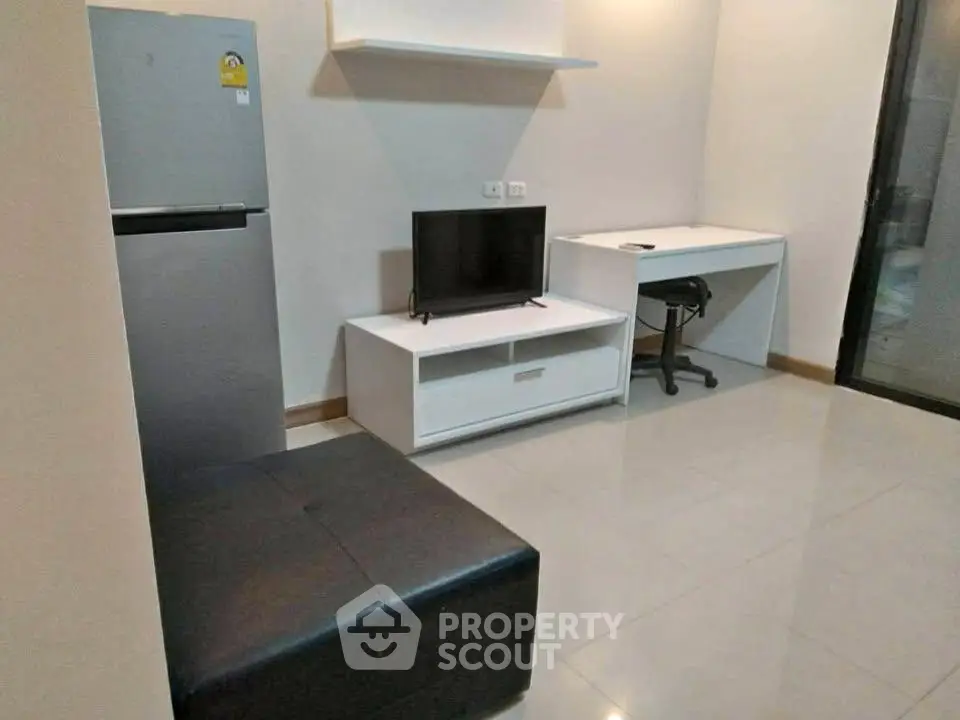 Modern living room with sleek furniture and compact design, featuring a TV, desk, and refrigerator.