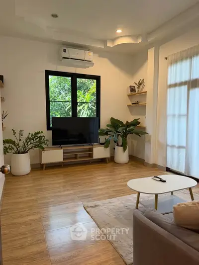 Charming living room with wooden flooring, modern decor, and lush greenery view.