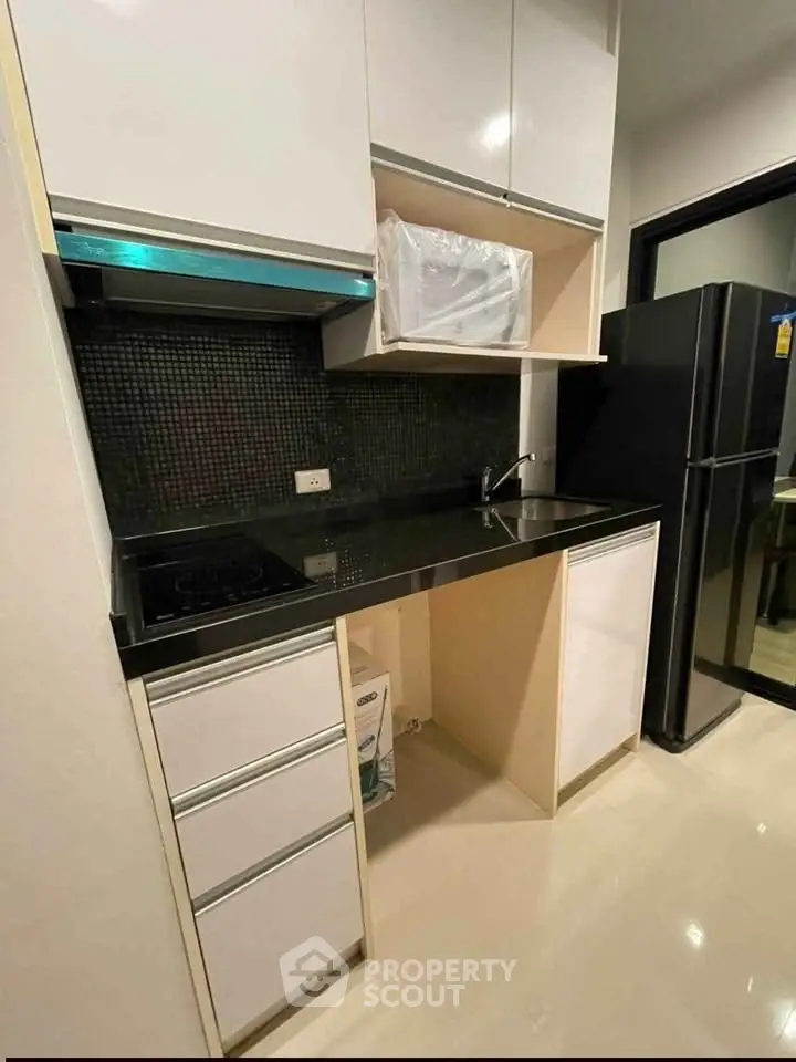 Modern kitchen with sleek black countertops and white cabinetry, featuring a built-in stove and spacious fridge.
