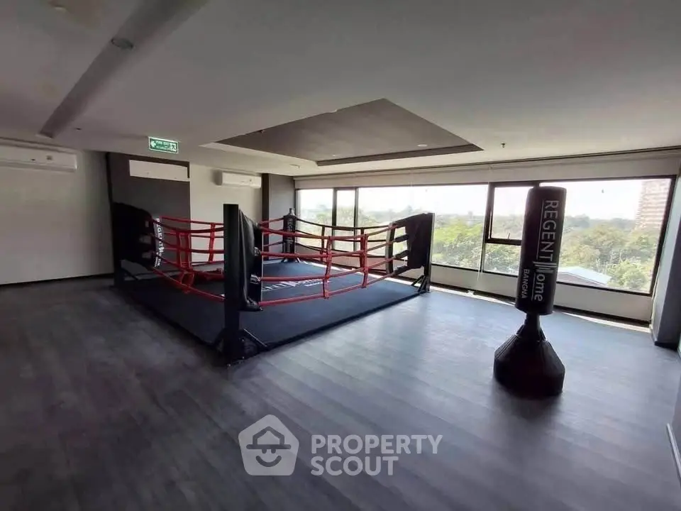 Spacious gym with boxing ring and punching bag, featuring large windows with scenic views.