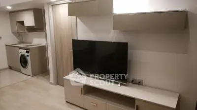 Modern living room with sleek TV unit and integrated washing machine in compact kitchen area.