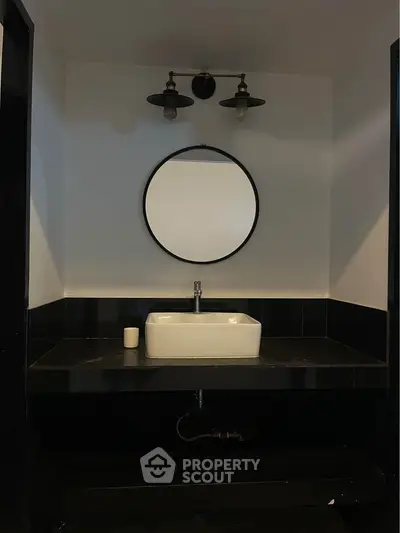 Modern bathroom with stylish black and white design featuring round mirror and elegant lighting.