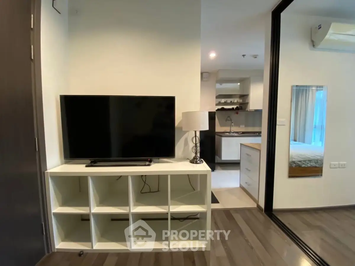 Modern apartment interior with TV, open kitchen, and cozy bedroom view.