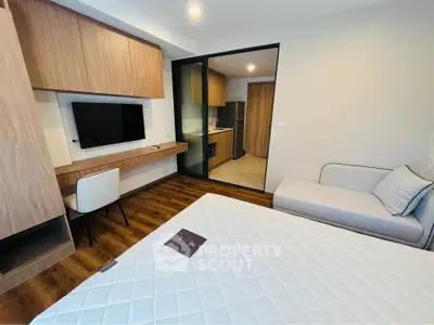 Modern bedroom with wooden flooring, built-in TV, and open view to kitchen area.