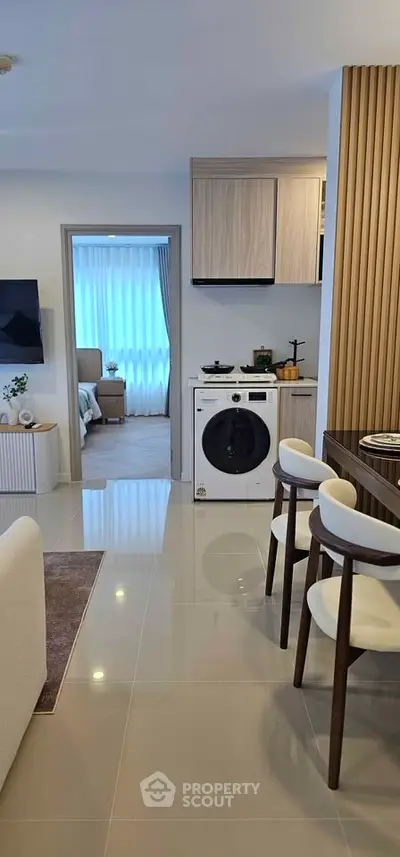 Modern open-plan living area with sleek kitchen and washing machine, leading to a cozy bedroom.