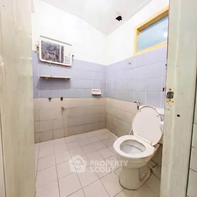 Spacious bathroom with tiled walls and floor, featuring a toilet and mirror, ideal for renovation.
