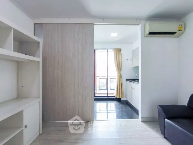 Modern apartment with sliding door, built-in shelves, and compact kitchen area.