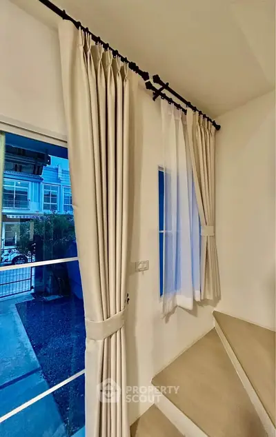 Elegant staircase with modern curtains and window view in a stylish home interior.