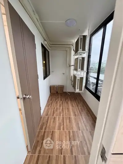 Compact storage room with wooden flooring and large windows in modern apartment.
