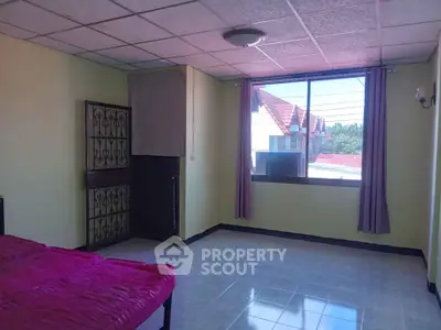 Spacious bedroom with large window and natural light, featuring tiled flooring and cozy ambiance.