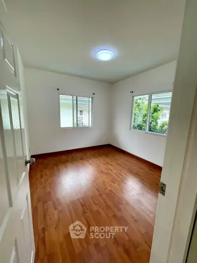 Spacious empty bedroom with wooden flooring and large windows for natural light.