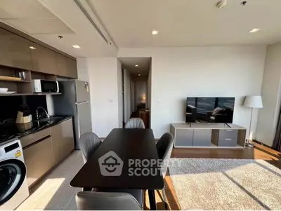 Modern open-plan living room with kitchen, dining area, and large TV, featuring sleek furniture and ample natural light.