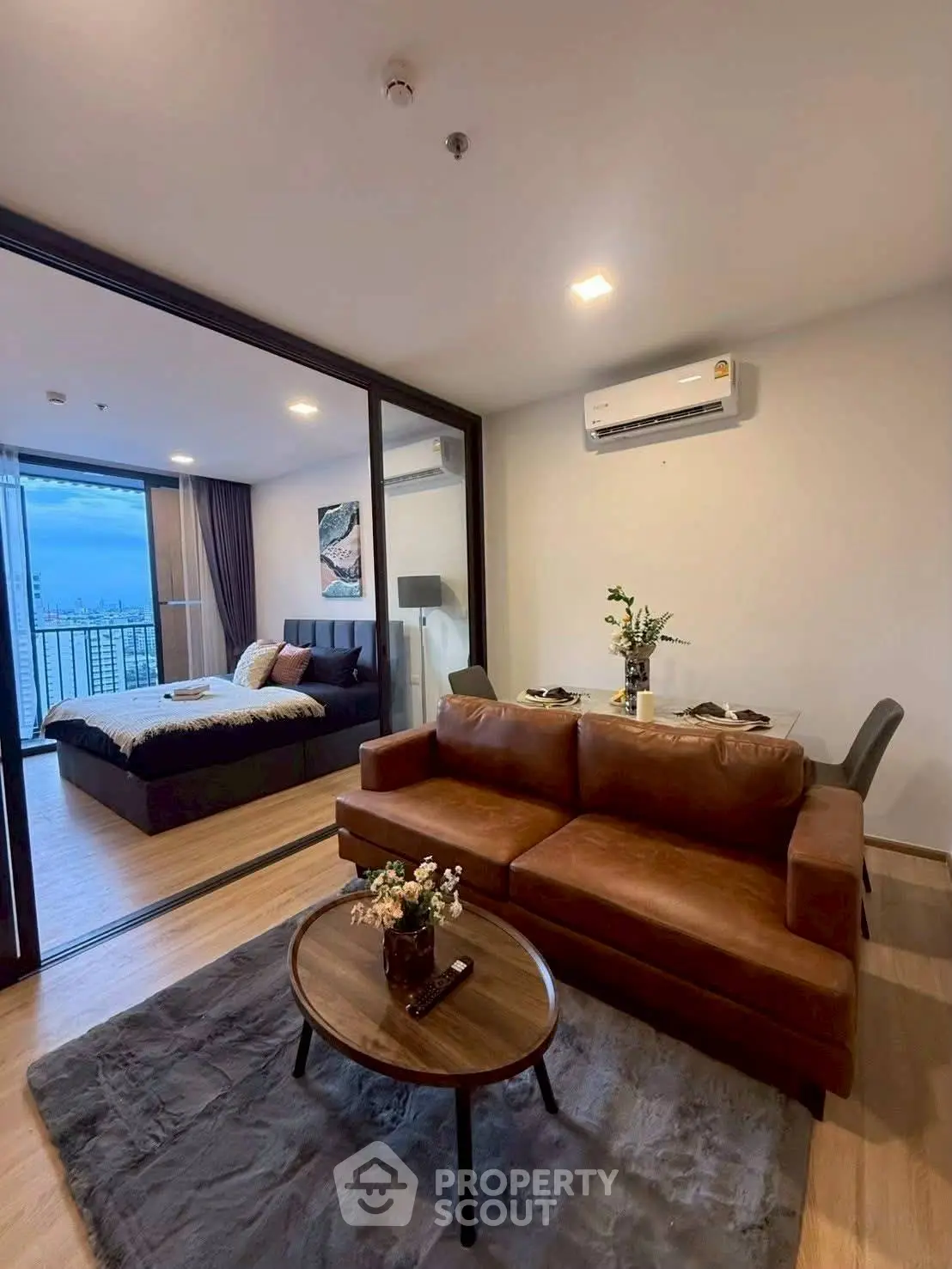 Modern open-plan living room with cozy seating and bedroom view, featuring stylish decor and cityscape balcony.