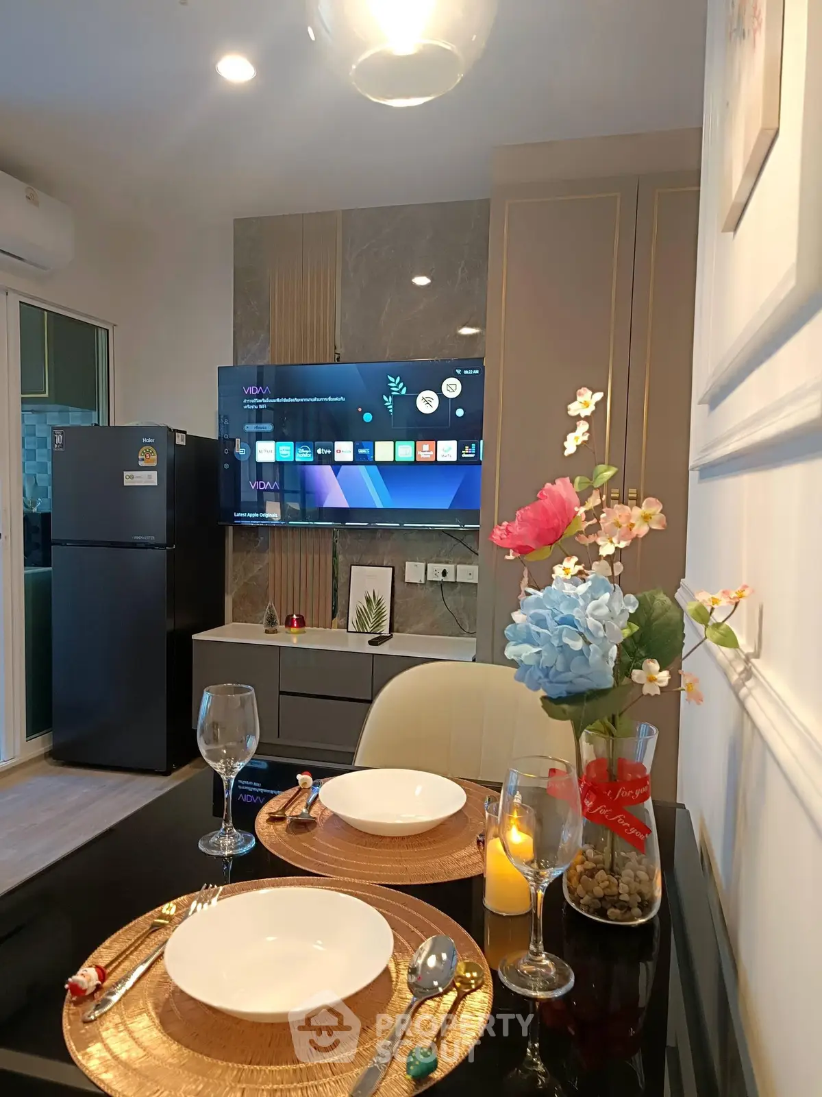 Modern dining area with elegant table setting and wall-mounted TV in stylish apartment.