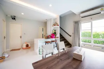 Modern open-plan living area with dining table, kitchen island, and staircase in bright, airy home.