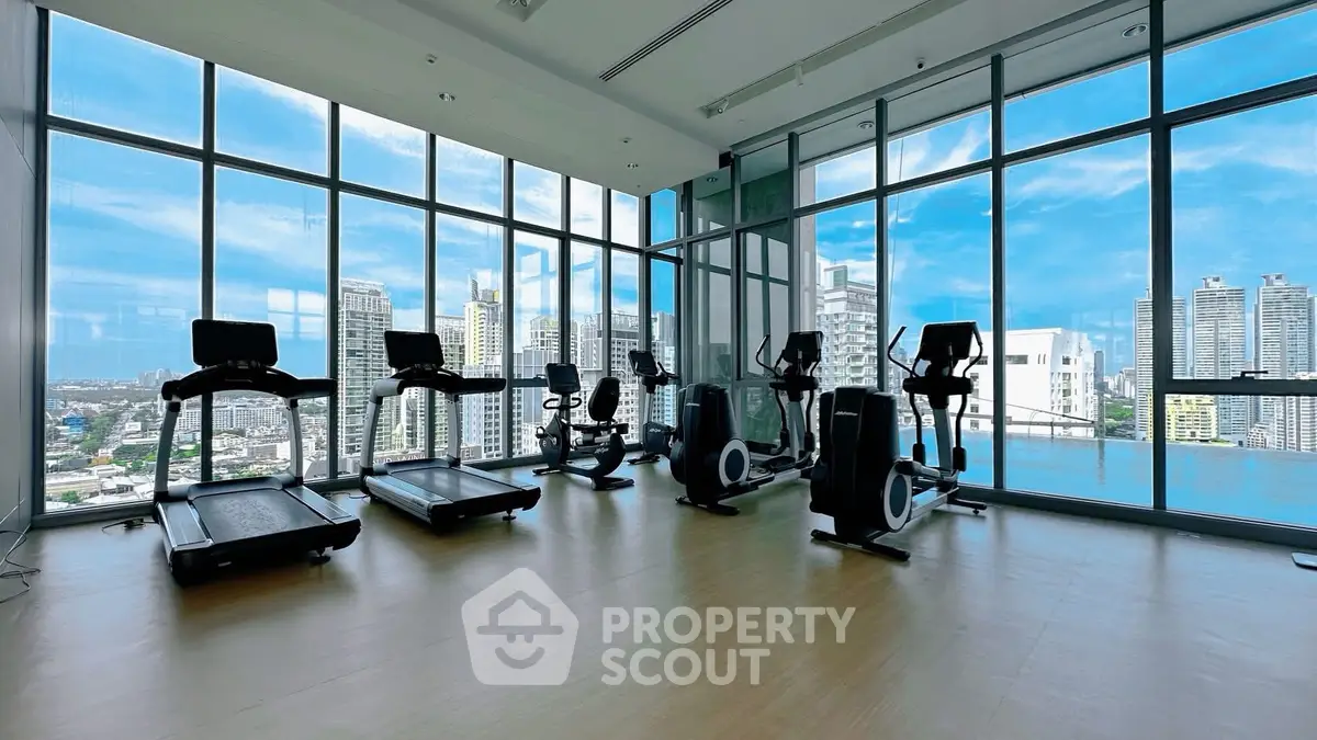Spacious gym with city view and modern exercise equipment in high-rise building.