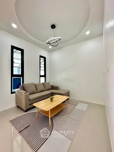 Modern living room with stylish sofa and geometric rug, featuring contemporary lighting and large windows.