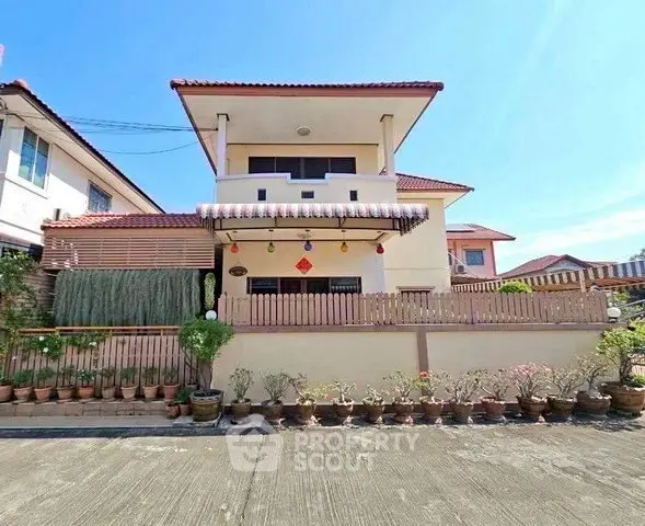 Charming two-story house with a red-tiled roof and decorative plants in a serene neighborhood.