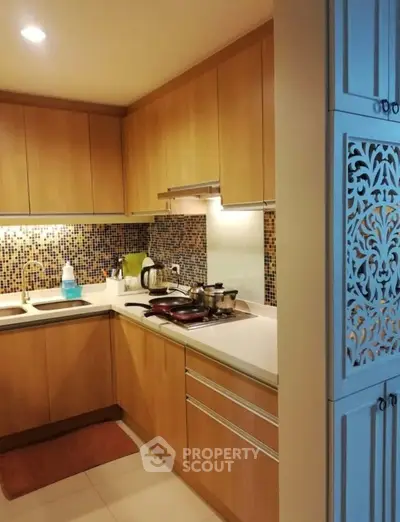 Modern kitchen with wooden cabinets and mosaic backsplash in cozy apartment.