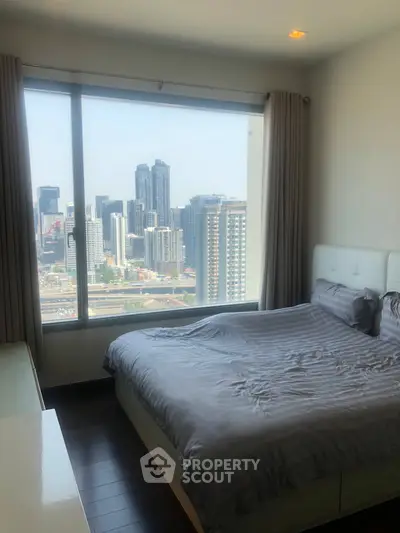 Modern bedroom with stunning city view from large window, featuring sleek furnishings and cozy bedding.