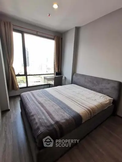 Modern bedroom with large window offering city view, featuring a cozy bed and stylish decor.