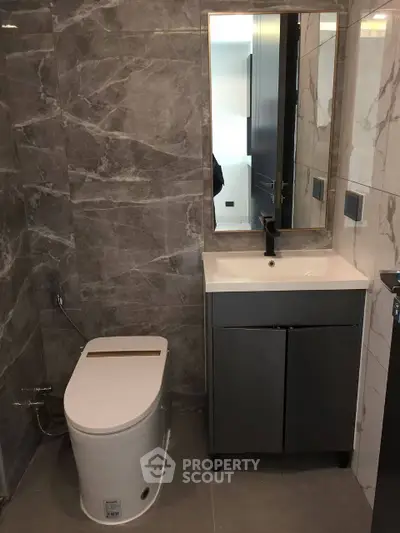 Modern bathroom with sleek design and marble tiles, featuring a stylish vanity and contemporary toilet.