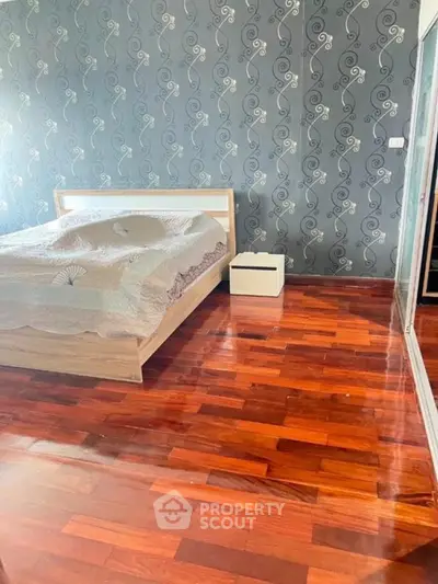 Spacious bedroom with elegant wooden flooring and stylish wallpaper, perfect for modern living.