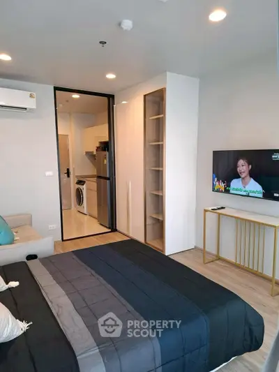 Modern studio apartment with sleek design, featuring a cozy bed, wall-mounted TV, and compact kitchen with washing machine.