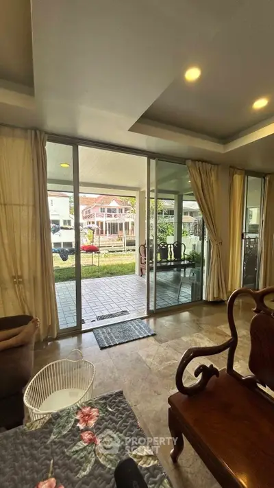 Spacious living room with large glass doors opening to a garden view, featuring elegant wooden furniture.