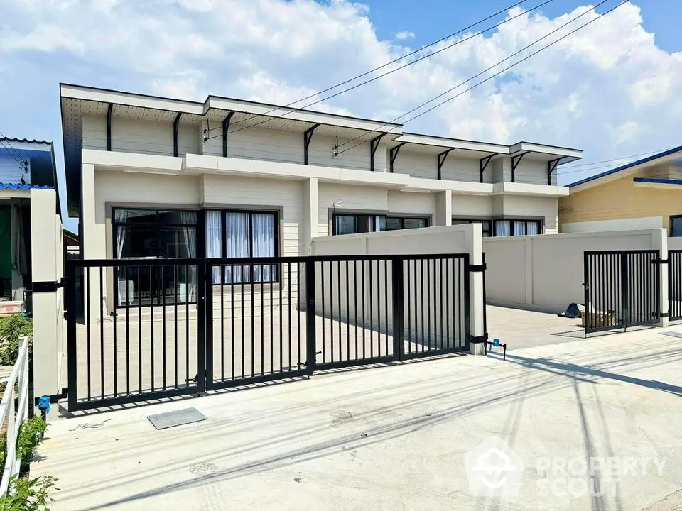 Modern townhouse exterior with sleek design and gated entrance under clear blue sky.