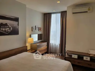 Cozy bedroom with modern decor and natural light, featuring wooden furniture and wall art.