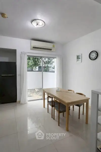 Bright dining area with modern table, chairs, and air conditioning, featuring a sliding glass door to a small balcony.