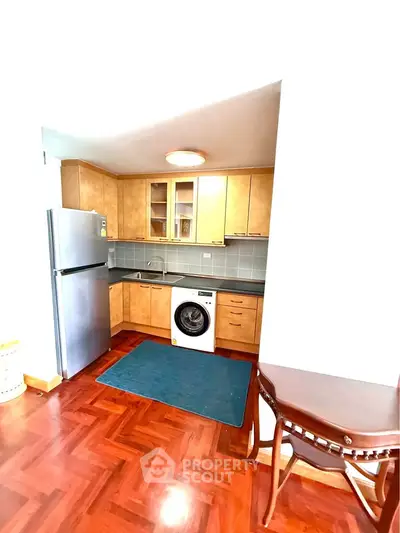 Modern kitchen with wooden cabinets, fridge, and washing machine in cozy apartment.