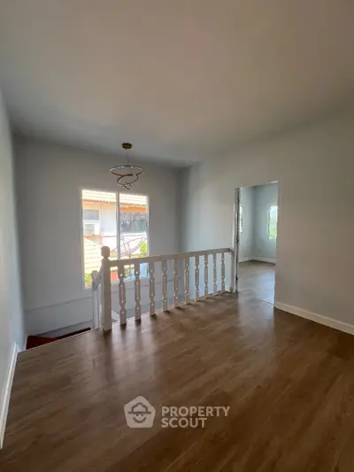 Spacious and well-lit upper-level living area with polished hardwood floors, elegant white balustrade, and a classic chandelier, offering a blank canvas for personalized interior design.