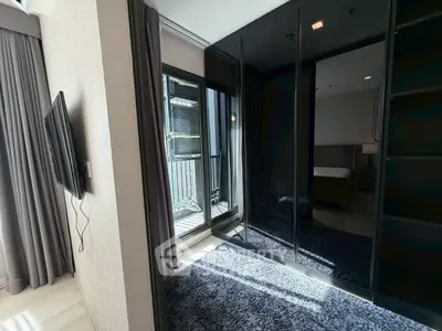 Modern bedroom with sleek black wardrobe and balcony access, featuring a wall-mounted TV and plush carpet.