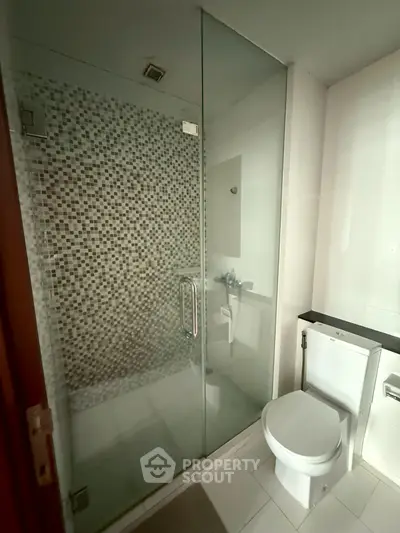 Modern bathroom with glass shower and mosaic tiles, featuring sleek design and contemporary fixtures.