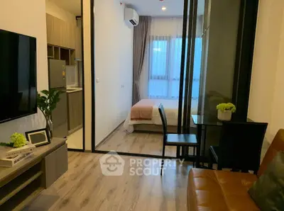 Modern studio apartment with open layout, featuring a cozy living area and bedroom separated by glass doors.