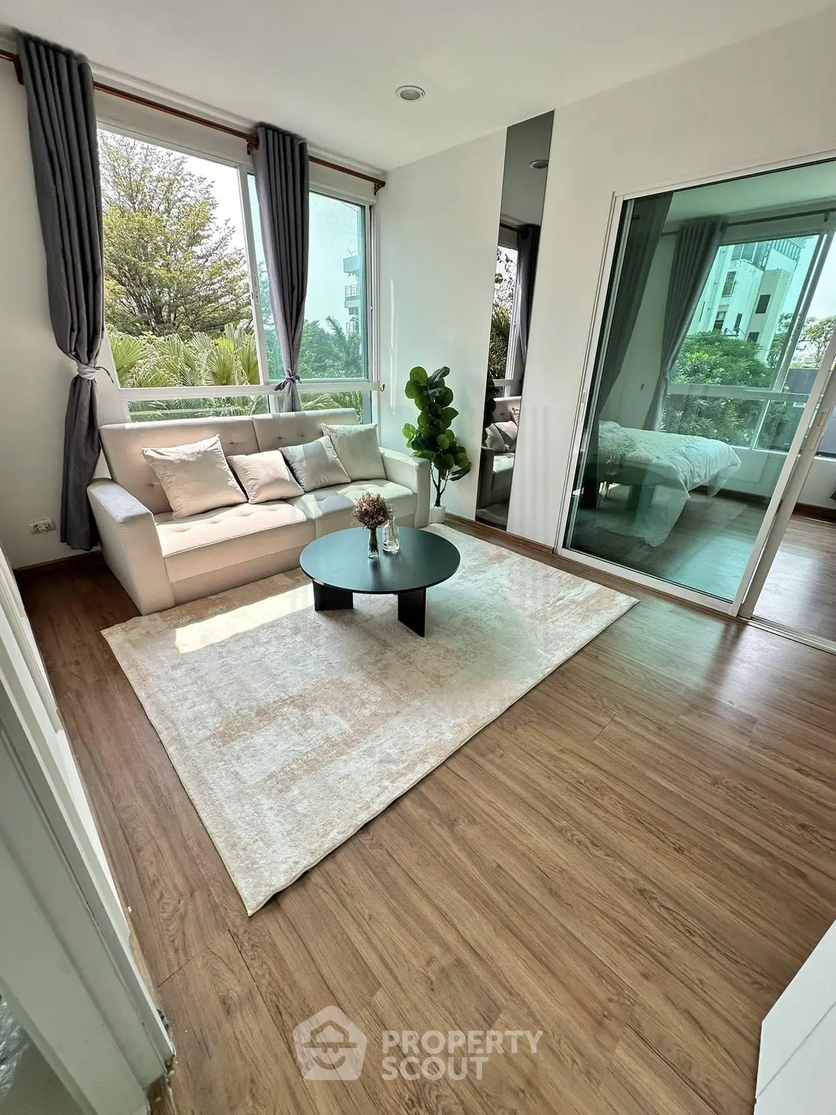 Modern living room with large windows and cozy decor, adjacent to a bedroom with glass sliding doors.