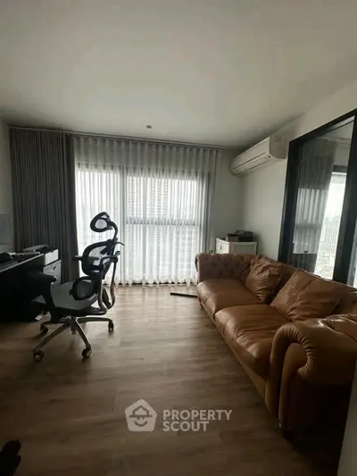 Modern study room with leather sofa and ergonomic chairs, featuring large window and wooden flooring.