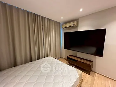 Modern bedroom with large TV and air conditioning, featuring wooden flooring and elegant curtains.