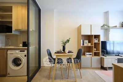 Modern open-plan living room with dining area and washing machine, featuring sleek furniture and natural light.