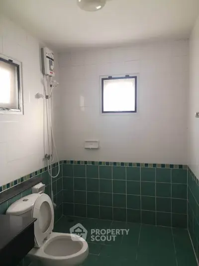 Spacious bathroom with green tiles and modern shower heater, ideal for comfort and relaxation.