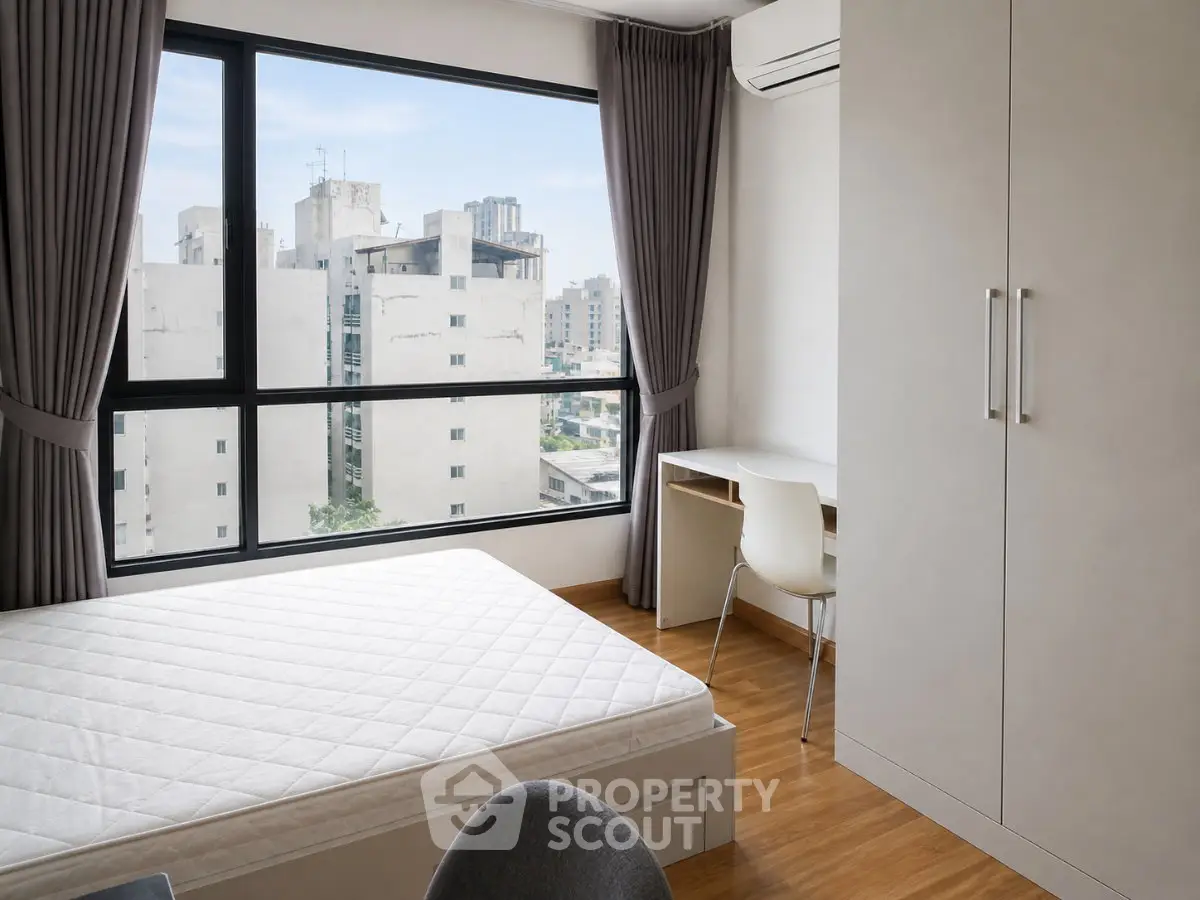 Modern bedroom with large window and city view, featuring a minimalist design and ample natural light.