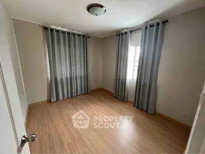 Spacious empty bedroom with wooden flooring and large windows for natural light.