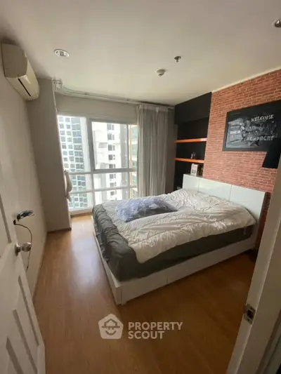 Modern bedroom with city view, featuring stylish brick accent wall and cozy bedding.