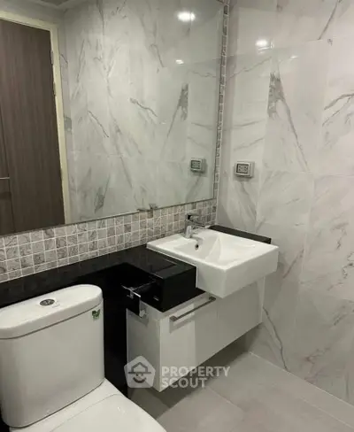 Modern bathroom with sleek fixtures and marble tiles, featuring a stylish sink and toilet.